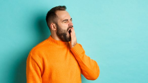 Photo of tired bearded man yawning, cover mouth with hand.